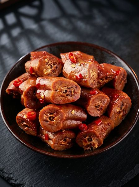 Bowl of spicy sausage pieces coated in red sauce on a dark table