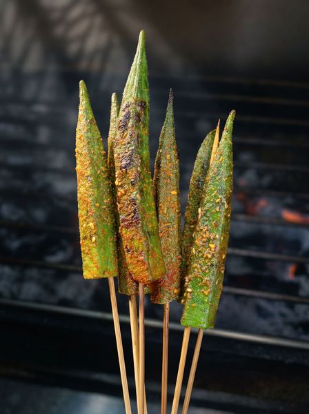 Grilled seasoned skewers over hot charcoal, with charred green and orange coating