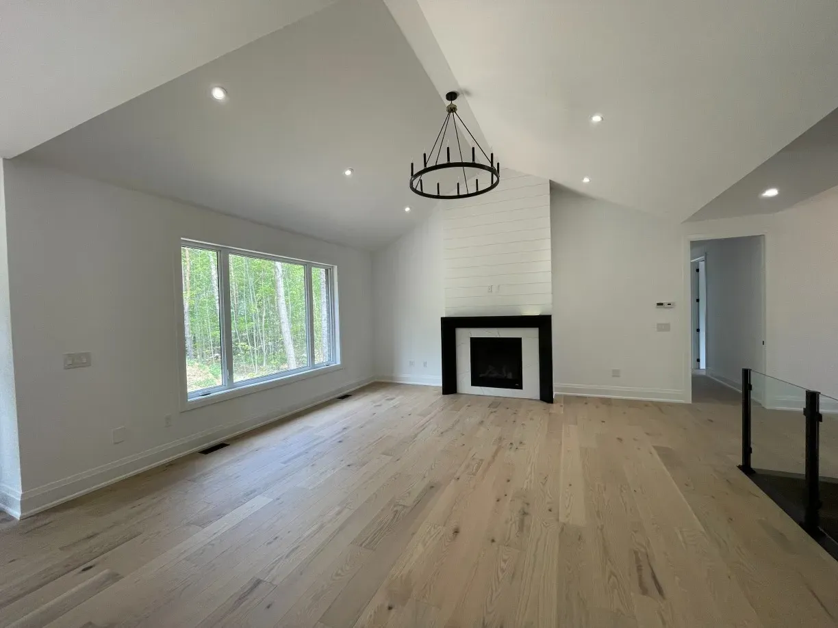 A bright, airy living room with a vaulted ceiling, a large green sofa, white armchairs, and a central fireplace.