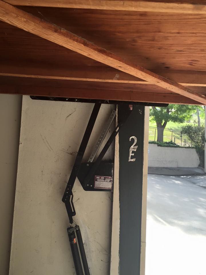 Garage door opener installed on a garage ceiling. Black arm and motor attached to the door.