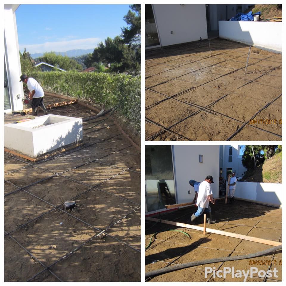 Workers preparing a backyard for concrete; rebar grid laid on the ground. White building in the background.