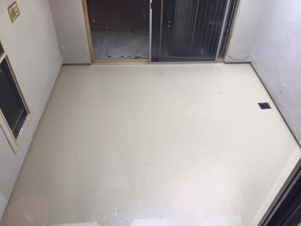 A small room with a freshly coated light gray floor. Open door leads outside.