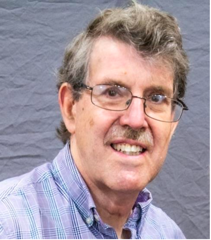 Man with glasses and mustache, wearing a purple plaid shirt, smiling at the camera.