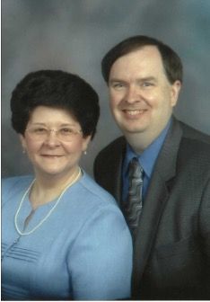 Couple smiling for a portrait. Woman in blue sweater, man in suit with a tie.