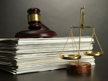 Mazo de madera, balanza de la justicia y pila de documentos sobre una superficie oscura.