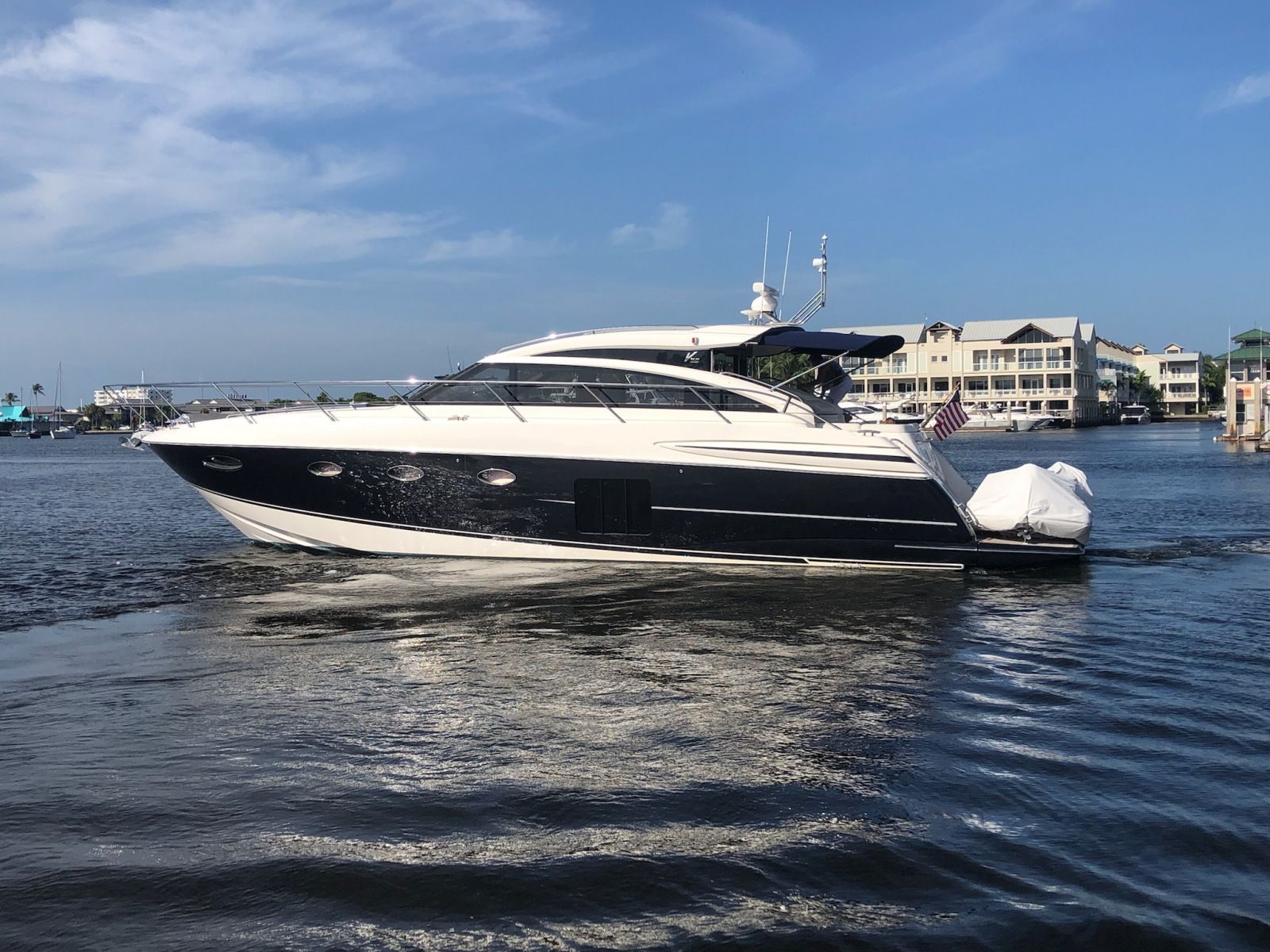 A sleek, dark blue and white motor yacht on a calm, blue body of water under a partly cloudy sky.