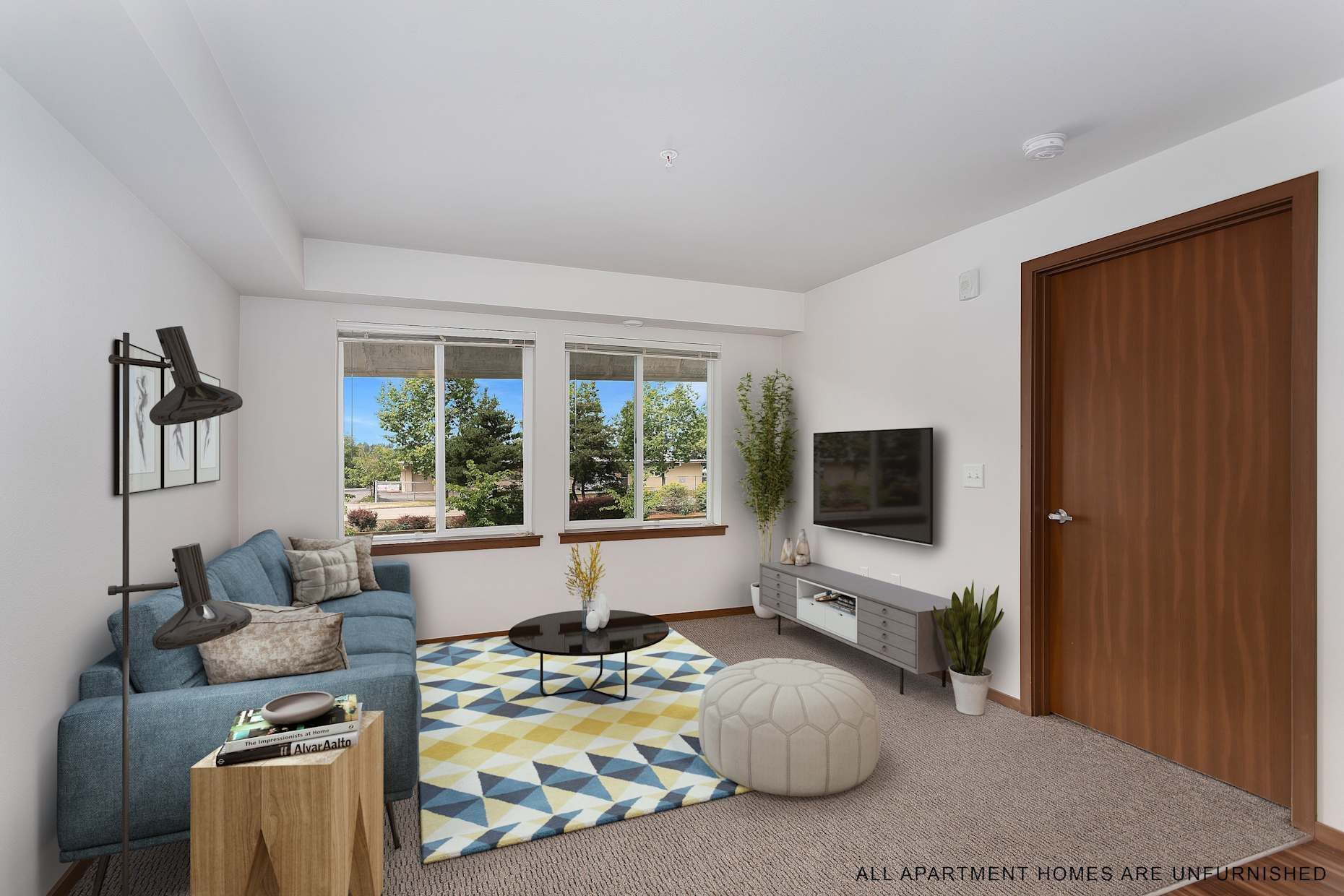 Living room with blue sofa, rug, coffee table, TV, and large windows.