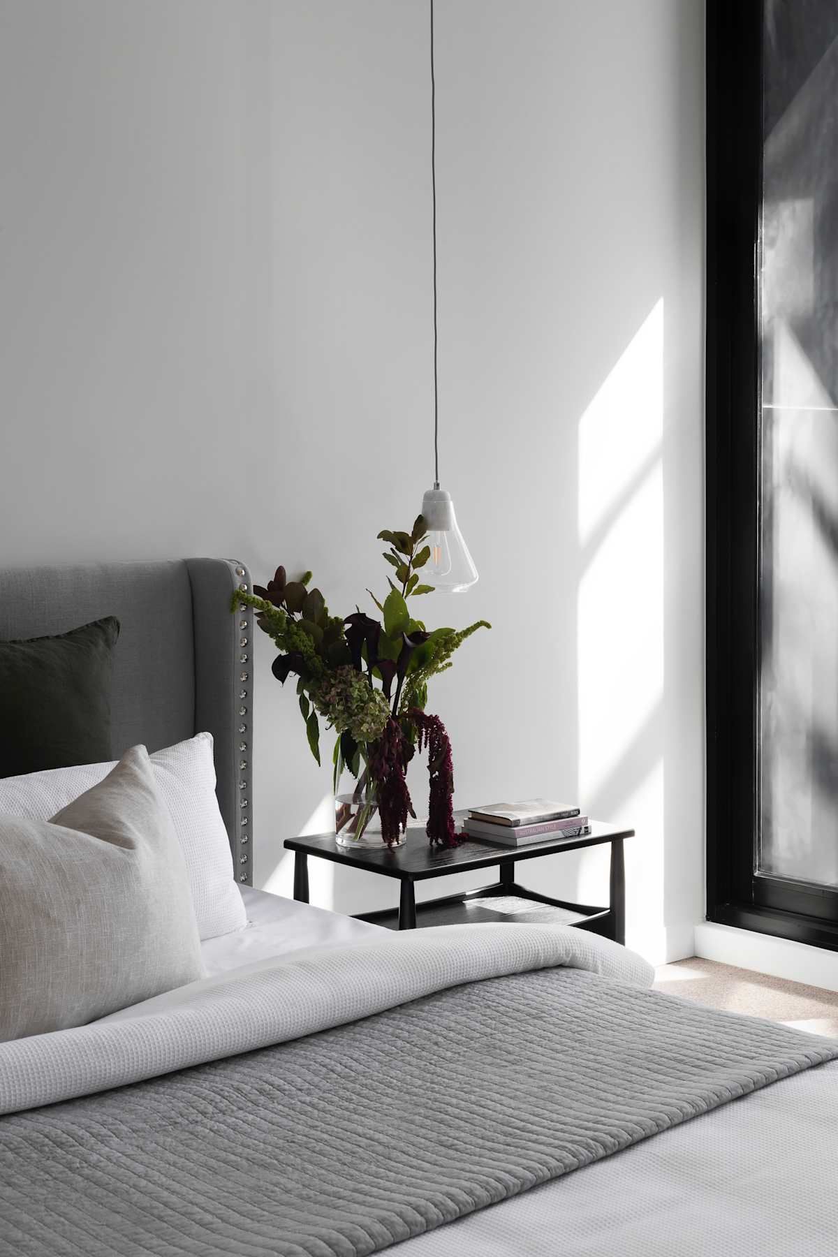 Bedroom scene with a bed, nightstand, vase of flowers, and pendant light.