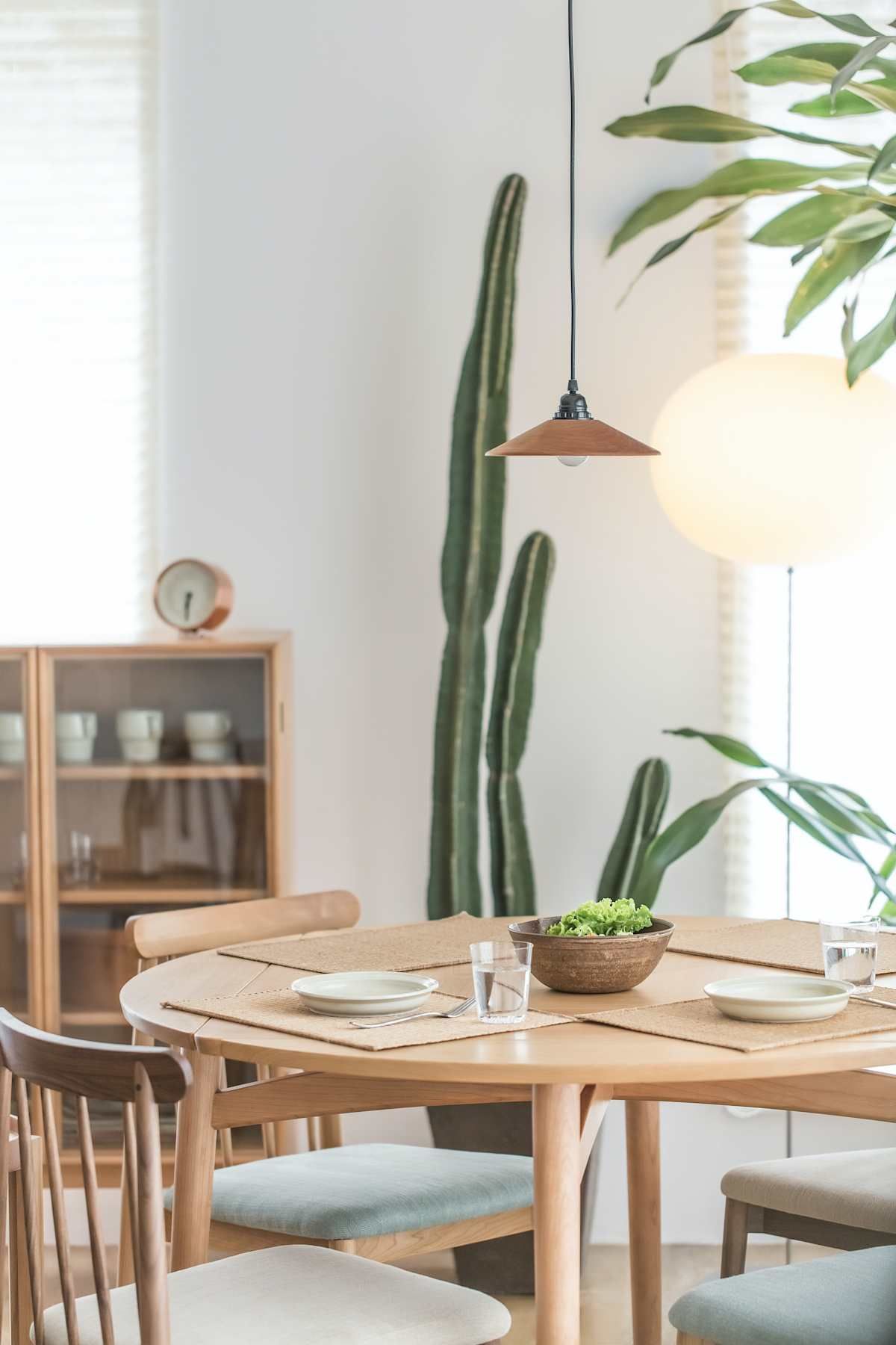 Dining room with round wooden table set for meal, large cactus, and pendant light.