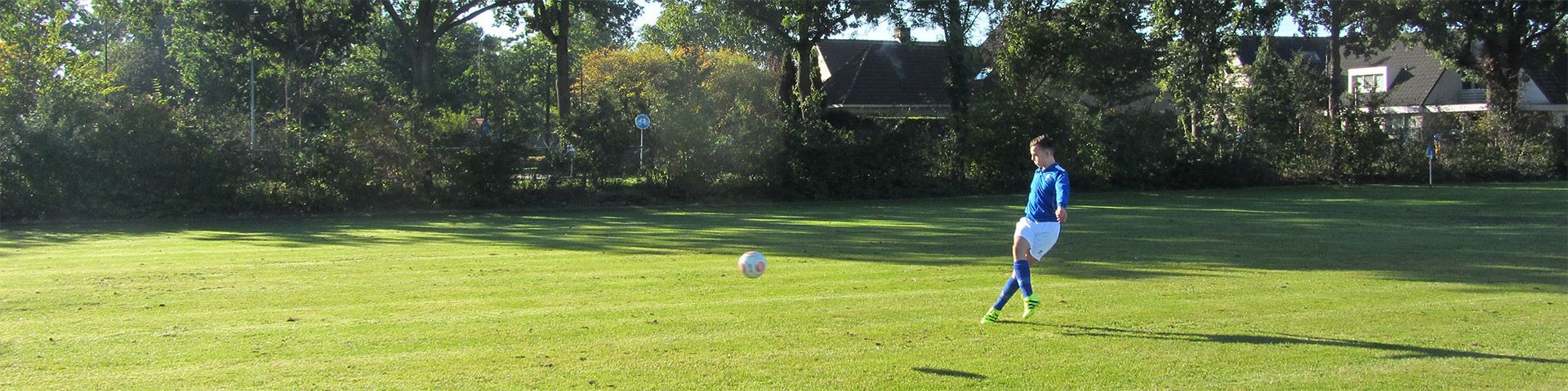 Een persoon in een blauw shirt schopt een voetbal op een veld.