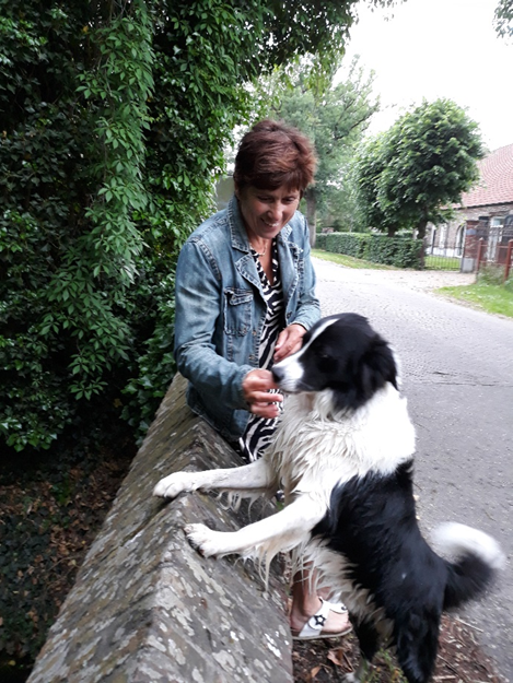 Een vrouw zit op een stenen muur naast een zwart-witte hond.