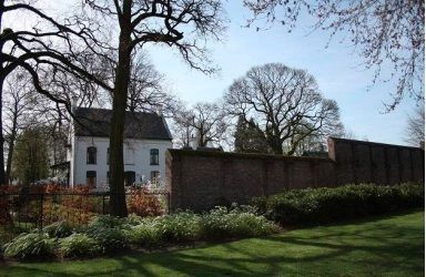 Een wit huis staat achter een bakstenen muur in een park