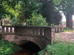 Een bakstenen brug over een beek in een park omgeven door bomen.