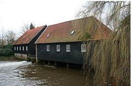 Een zwart gebouw met een rood dak staat naast een rivier.