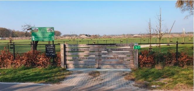 Een houten poort die naar een veld leidt met een bord aan de kant van de weg.