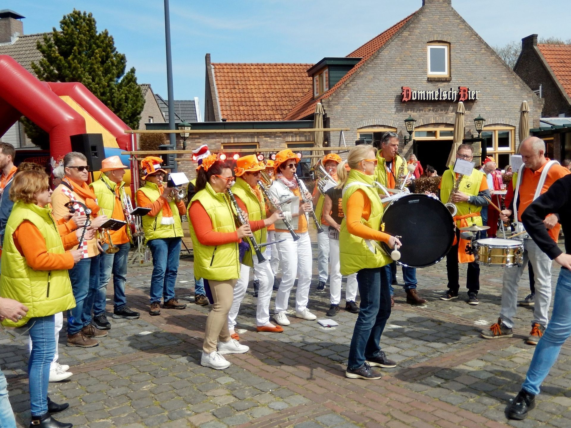 Een groep mensen in oranje vesten bespeelt instrumenten voor een gebouw met de tekst 'British'