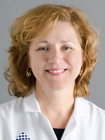 A woman in a white lab coat is smiling for the camera