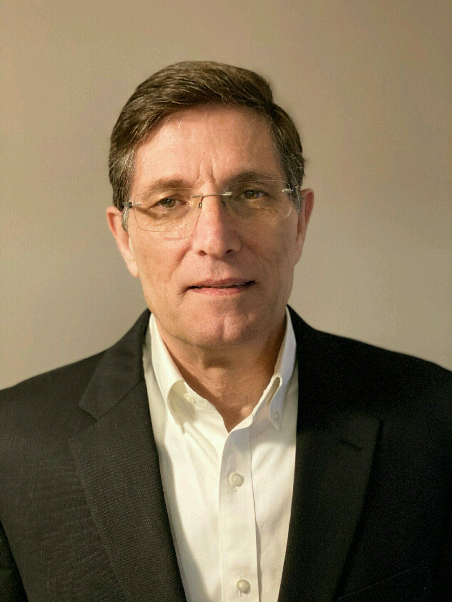 A man wearing glasses and a suit is smiling for the camera.