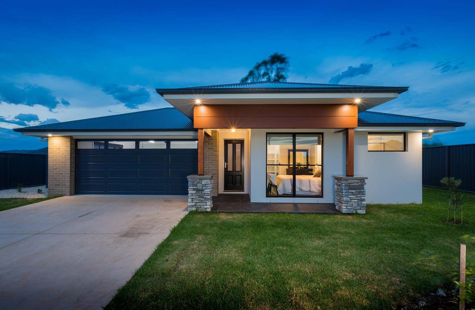 A White House With A Blue Roof Is Sitting On Top Of A Lush Green Lawn — Morphett Construction In Calala, NSW