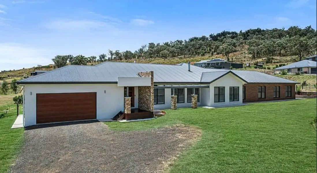 A Large White House With A Garage Is Sitting On Top Of A Lush Green Hillside — Morphett Construction In Calala, NSW
