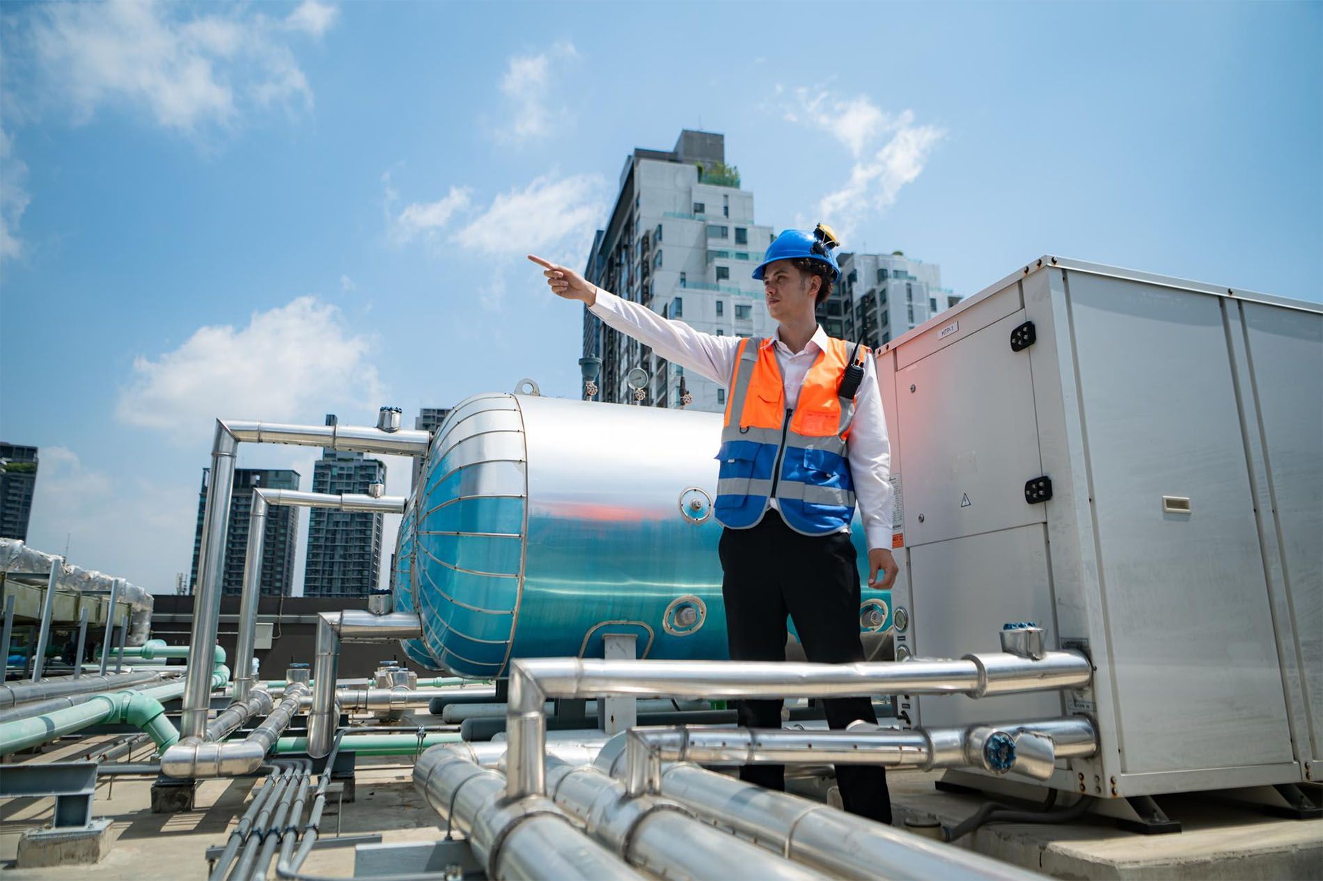 A man in a hard hat is pointing at something while standing on top of a building.