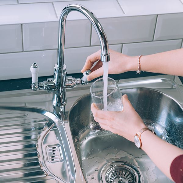 A person is pouring water into a glass in a kitchen sink