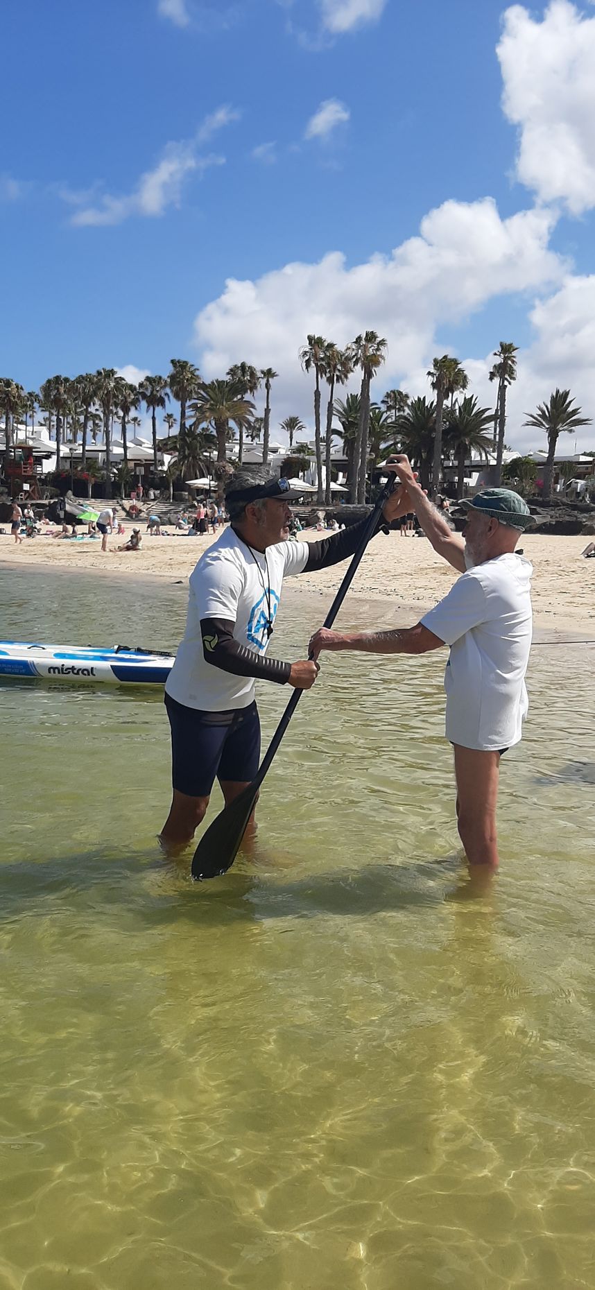 Two men are standing in the water holding paddles.