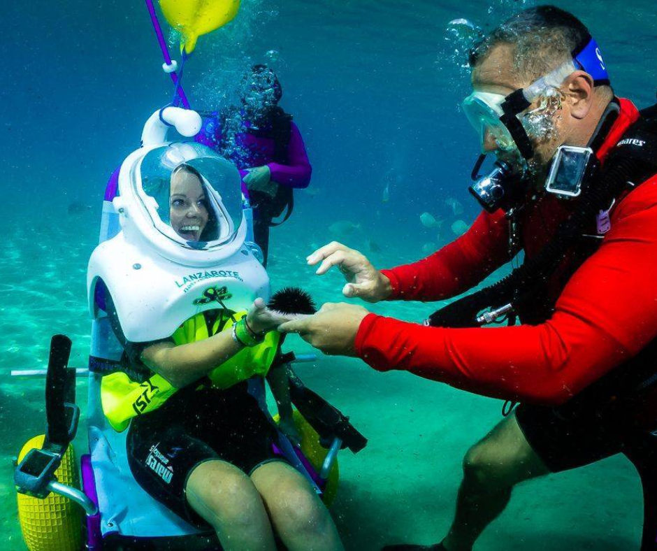 A woman in a wheelchair is being helped by a scuba diver