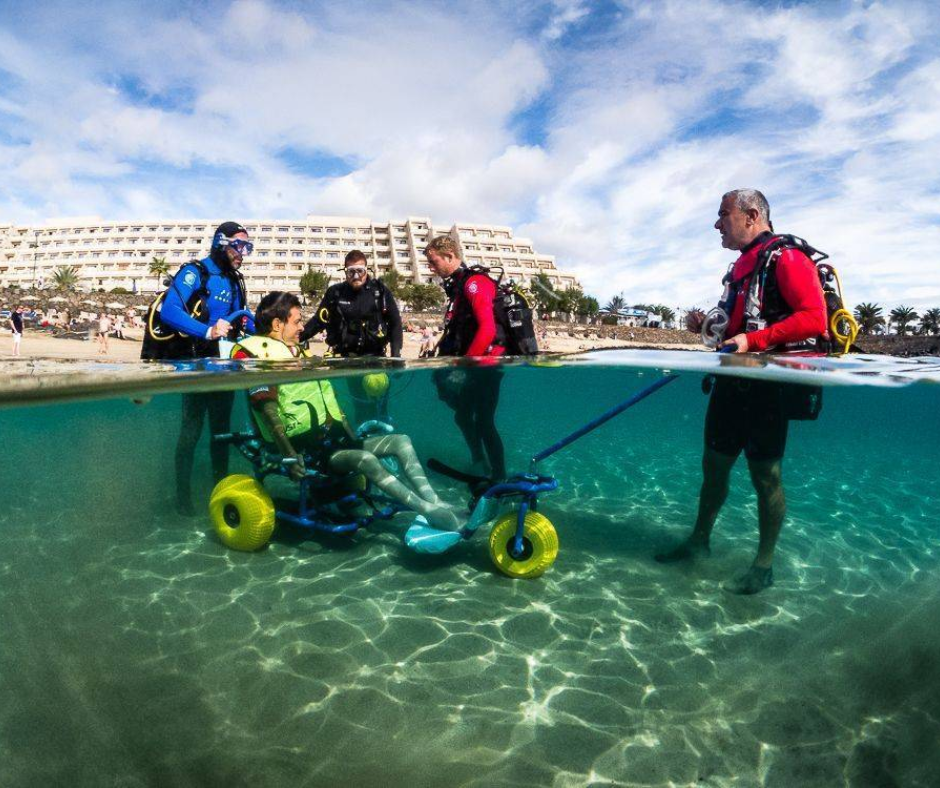 A person in a wheelchair is being pulled underwater by divers