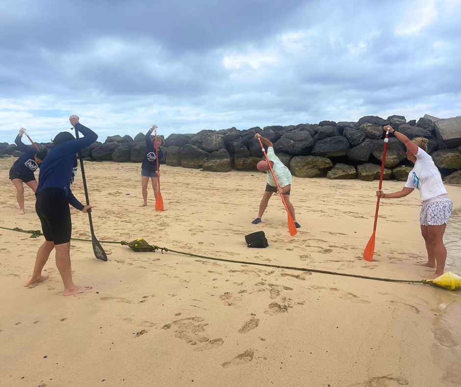 A group of people are standing on a beach holding paddles.