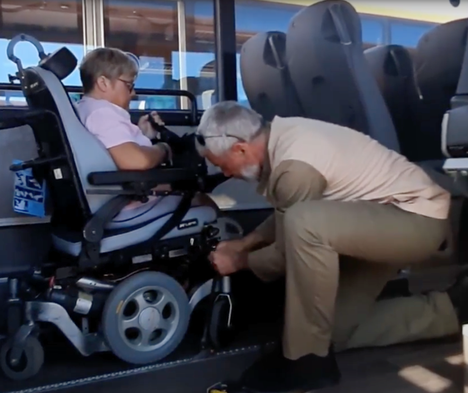 A man kneeling down next to a woman in a wheelchair helping to secure the seat