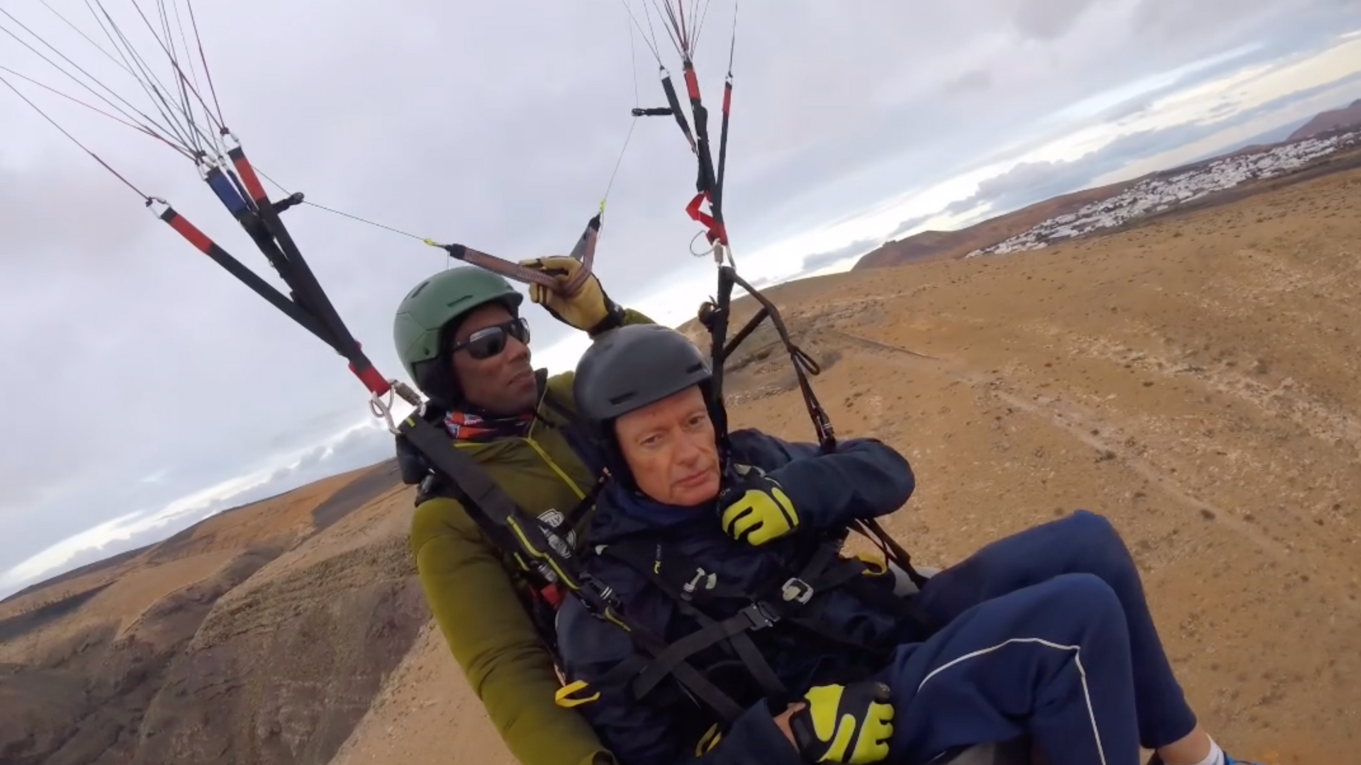 A man and a woman are flying a parachute over a desert.