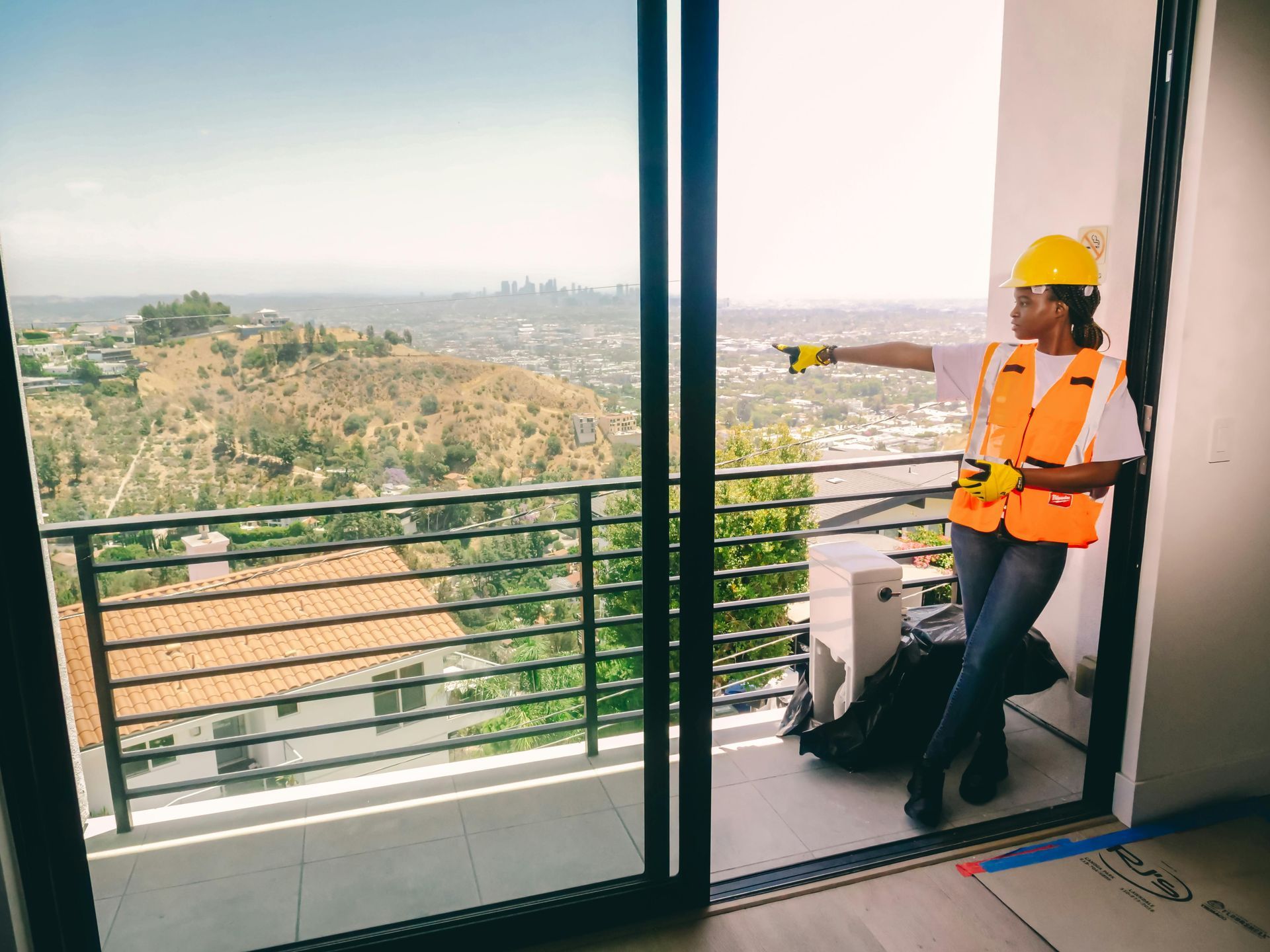 A construction worker is standing on a balcony with a view of a city.