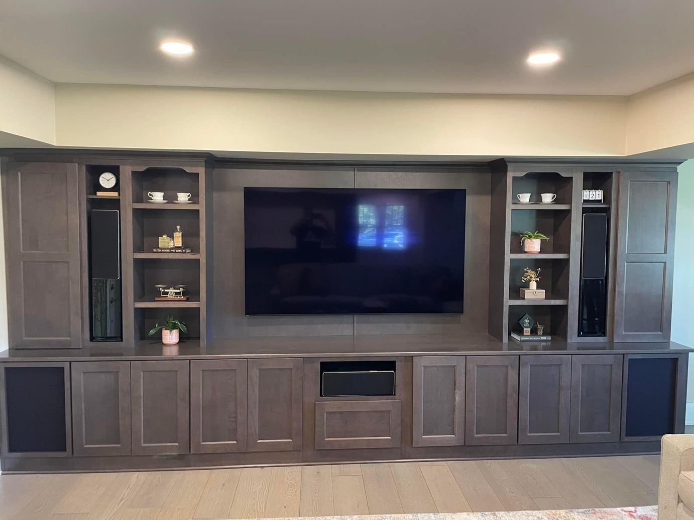 Built-in entertainment center with TV and cabinets, gray-brown wood, recessed lighting.