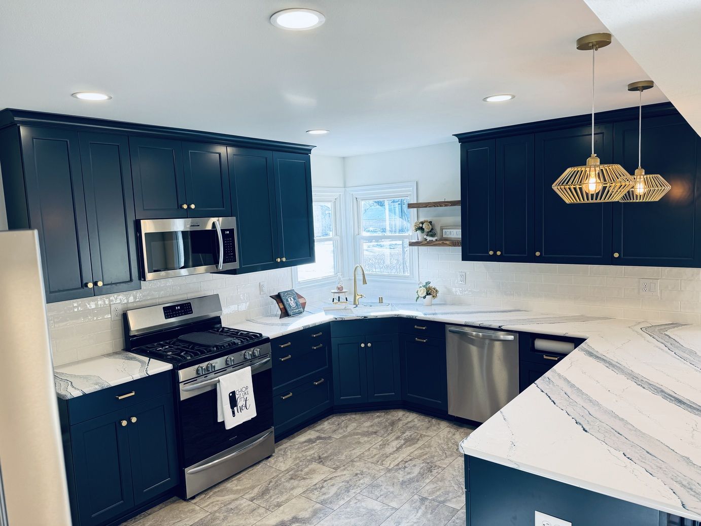 Navy blue kitchen with white countertops, stainless steel appliances, and gold pendant lights.