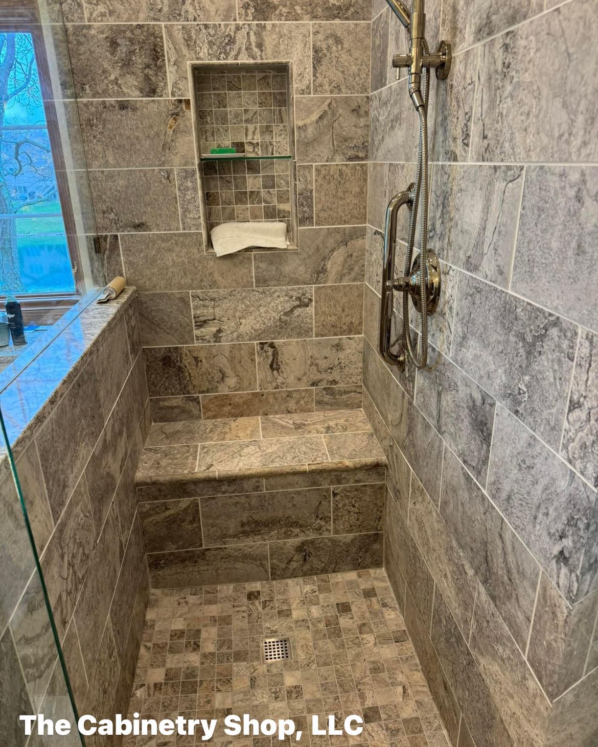 Shower with stone tile, built-in seating, niche, and antique-style shower fixtures.