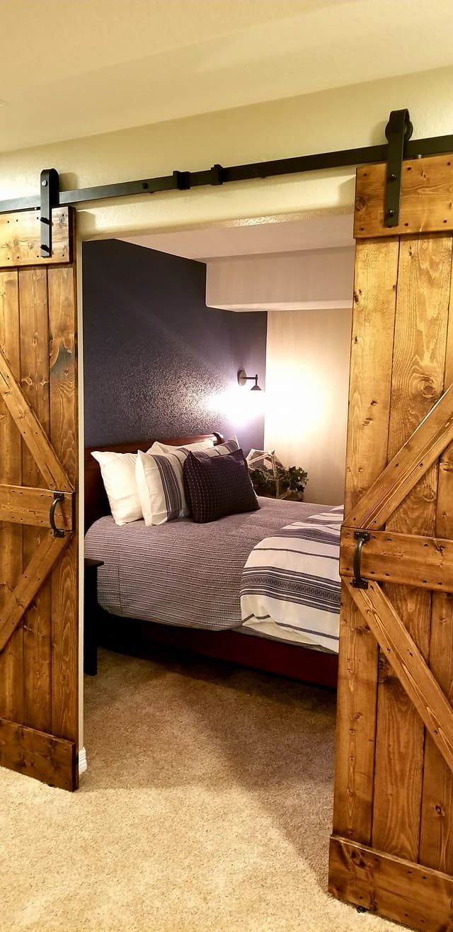 A view of a bedroom through open, rustic wooden barn doors, revealing a bed with dark and patterned bedding.