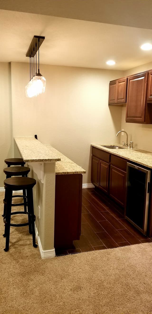 A kitchen area with brown cabinets, granite countertops, a bar counter with three stools, and pendant lights.