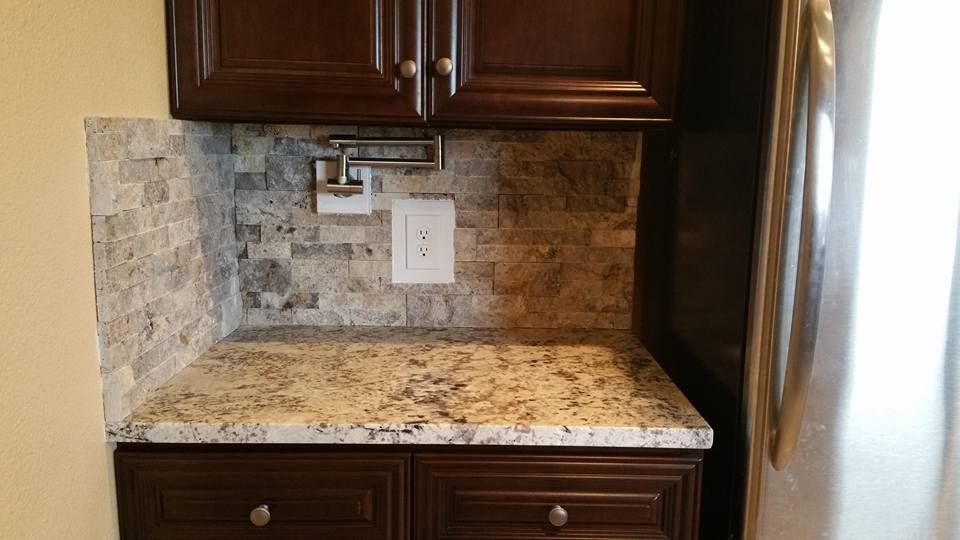 A kitchen counter with stone-tile backsplash, dark brown cabinets, a pot filler faucet, and a light-colored granite top.