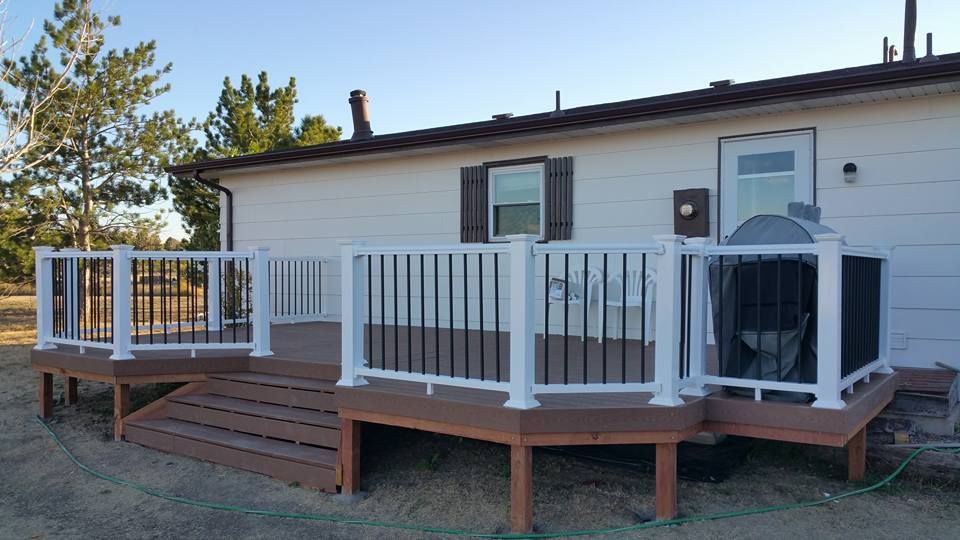 A light-colored house featuring a new brown deck with white railings and black balusters, plus a set of front steps.