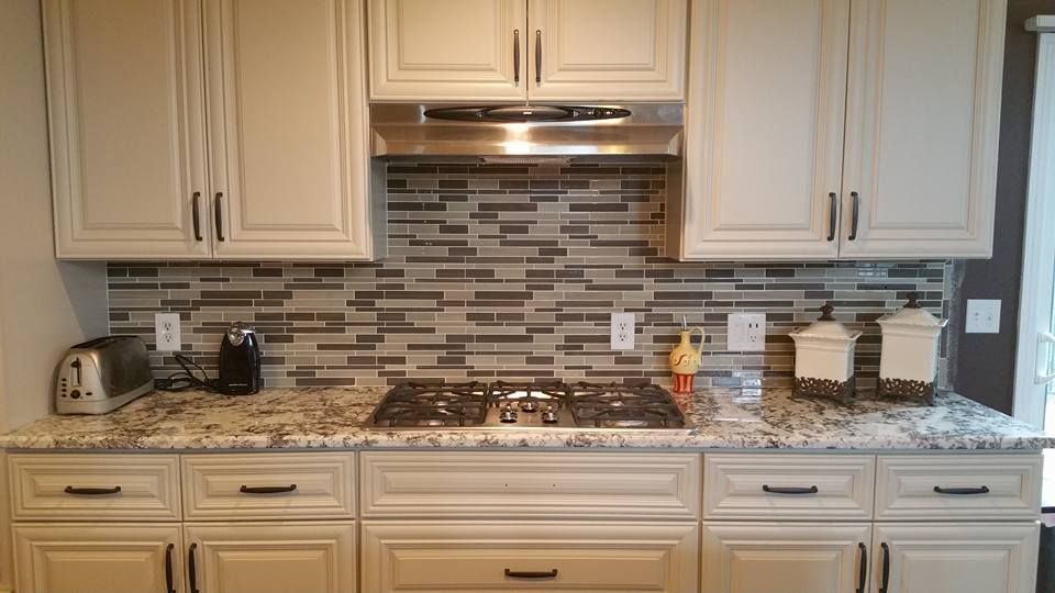 A kitchen counter with a gas stove, stainless steel range hood, stone backsplash, and cream-colored cabinets.