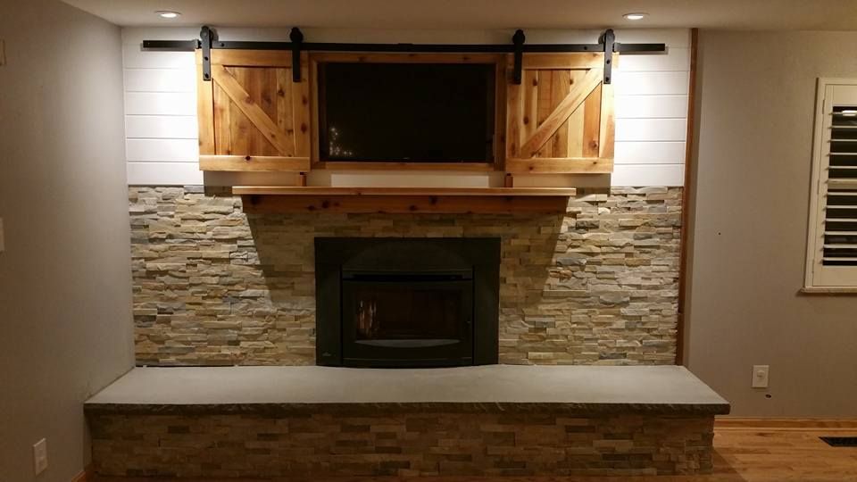 A fireplace with a stone facade, a wood mantel, and a television enclosed by sliding barn doors mounted on a shiplap wall.