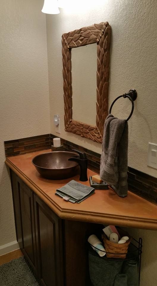 A bathroom vanity with a copper vessel sink, dark wood cabinets, a textured wood-frame mirror, and a gray hand towel.