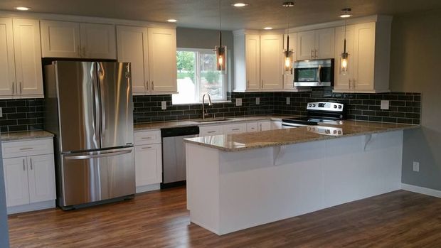 Modern kitchen with white shaker cabinets, stainless steel appliances, a large central island, and light wood-look flooring.