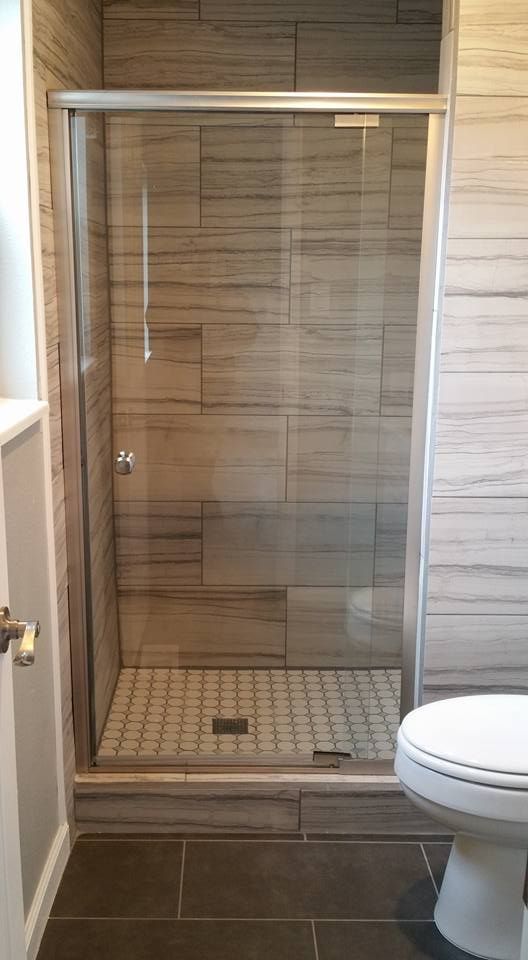 A shower stall with wood-look tile walls and a glass door, situated next to a white toilet in a tiled bathroom.