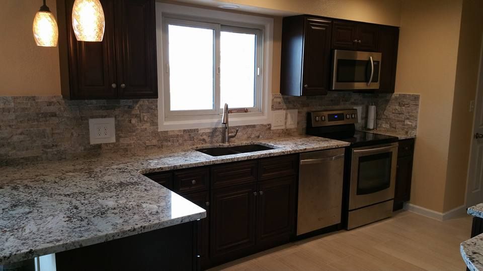 A modern kitchen with dark wood cabinets, speckled granite countertops, stainless steel appliances, and a tiled backsplash.
