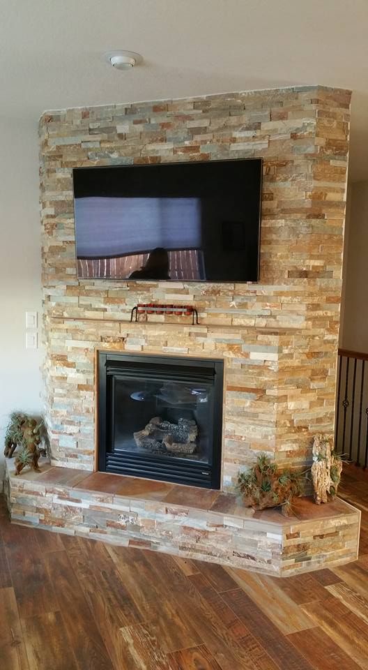 A flat-screen television mounted above a natural stone fireplace in a room with hardwood flooring.