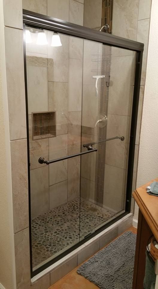 A walk-in shower with a glass door, dark metal frame, horizontal towel bar, and stone-tiled walls and floor.