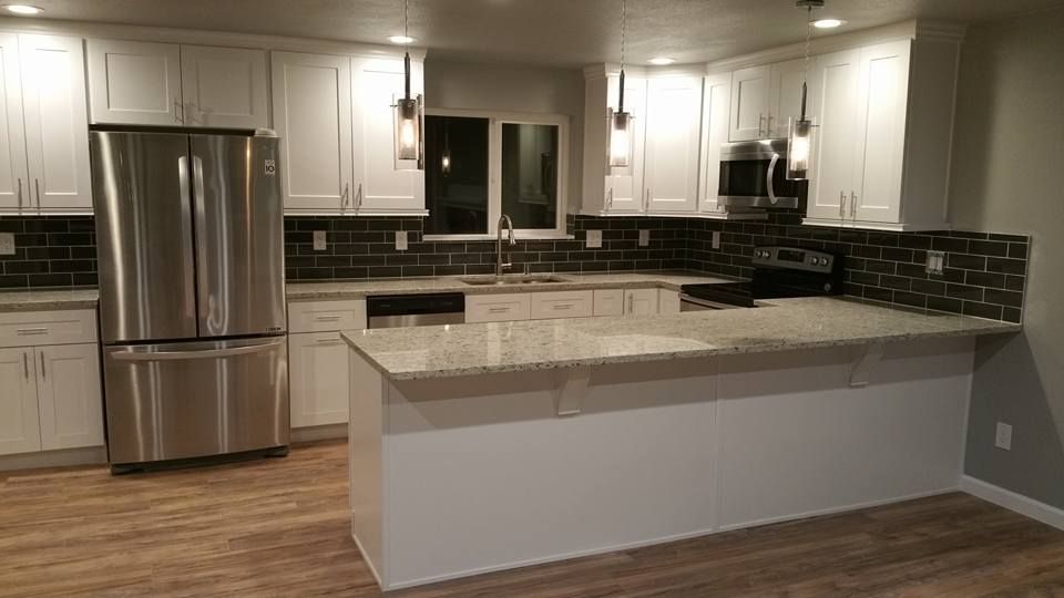 A renovated kitchen featuring white cabinets, stainless steel appliances, speckled countertops, and dark tiled backsplash.
