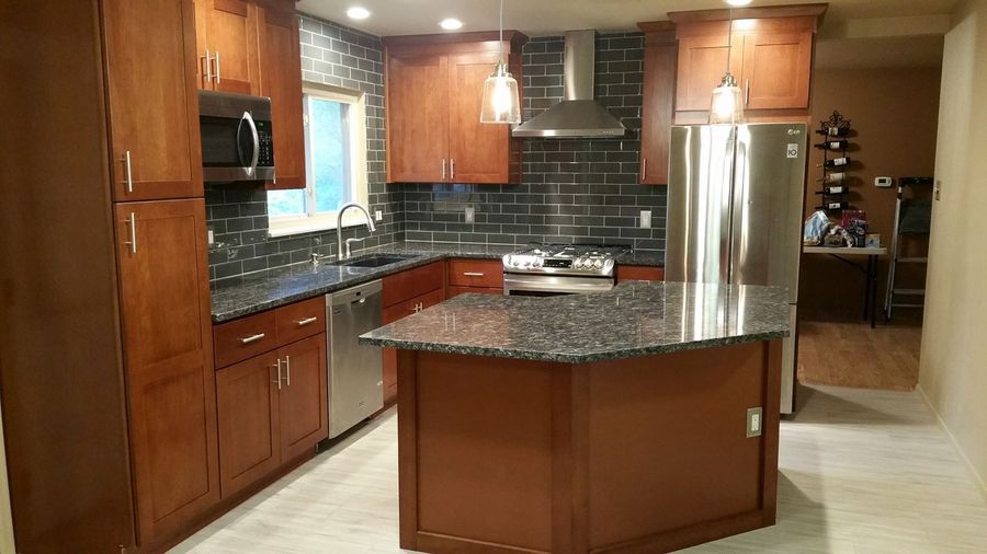 A bright, modern kitchen featuring white cabinets, gray wood-look flooring, a kitchen island, and a dining area window.